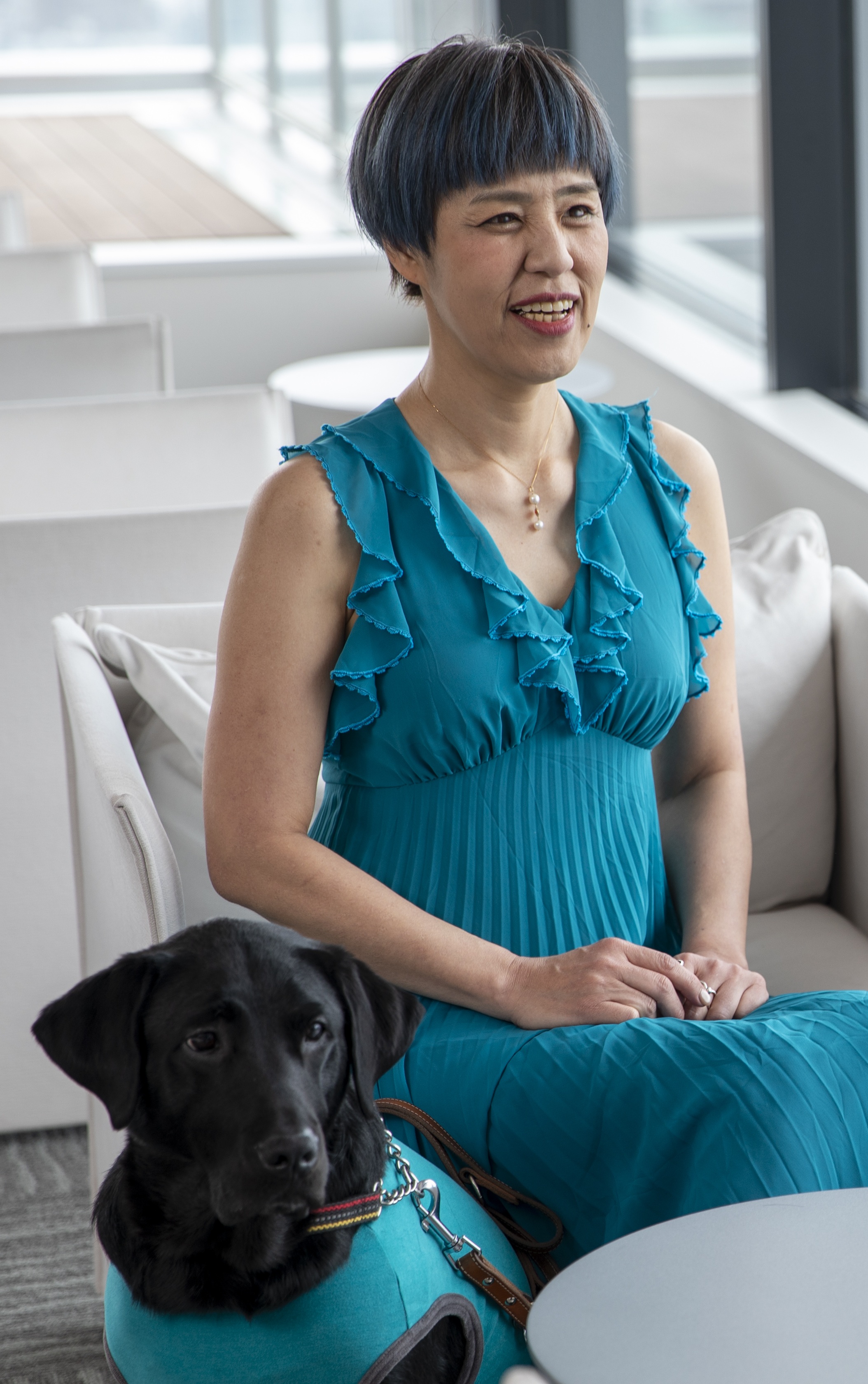 浅井純子がグリーン色のドレスを着て椅子に座っていて、その傍に盲導犬が座っている写真