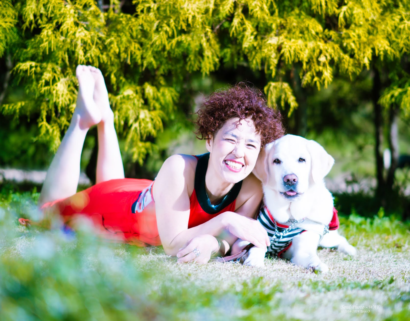 浅井純子と盲導犬の犬が芝のある所で寝転がりながら微笑む写真