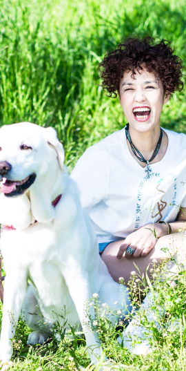 盲導犬のヴィヴィッドと一緒に草原に座りながら笑う浅井純子の写真